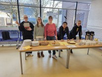 Fünf Schülerinnen und Schüler, die am Elterncafé stehen und Kuchen und Kaffee verkaufen.